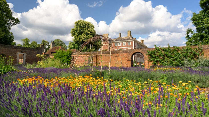 View of the house beyond the walls of the Kitchen Garden full of vibrant flowers at Ham House and Garden, Surrey